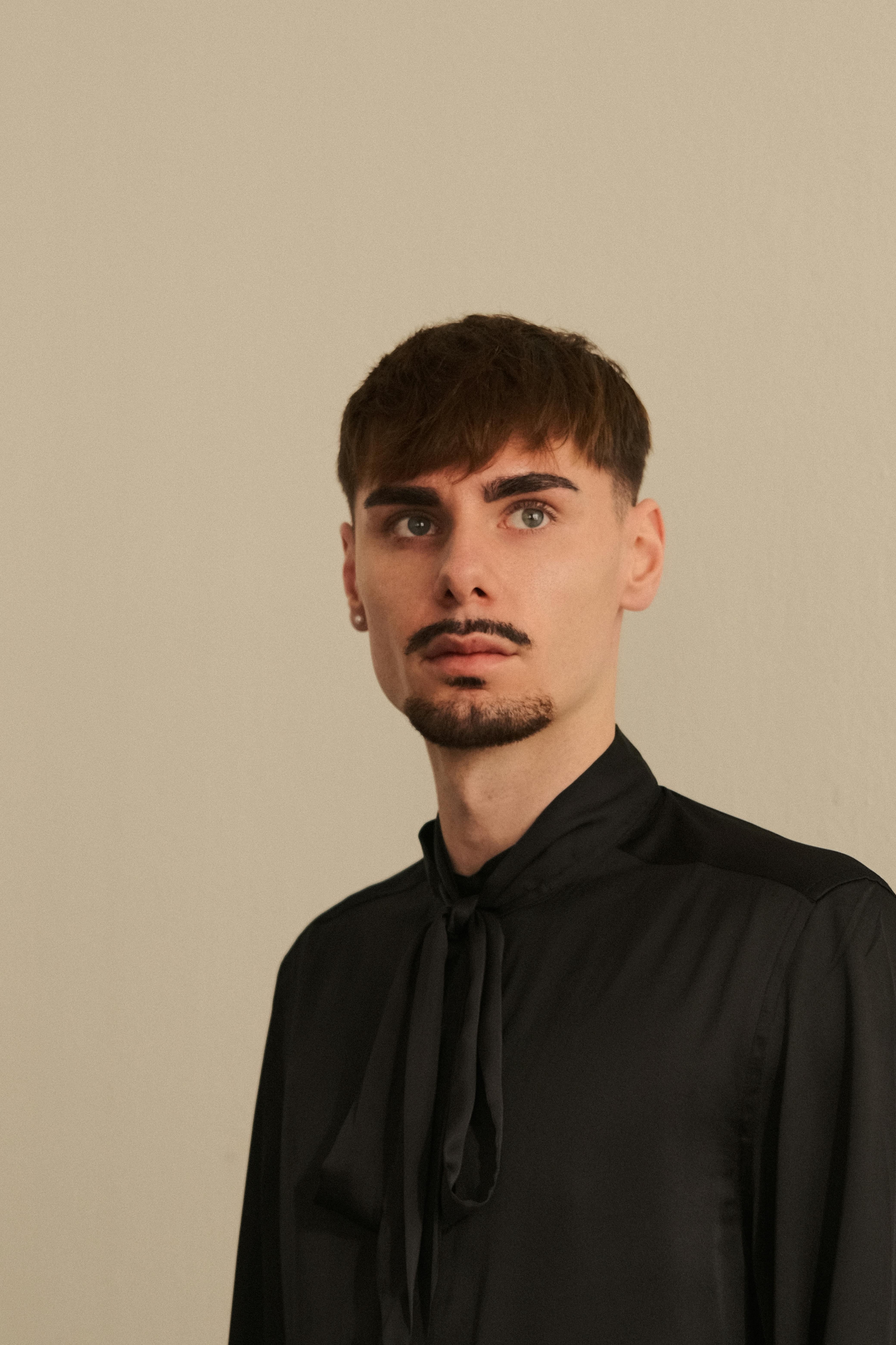 Ilmainen Tyylikäs muotokuva nuoresta miehestä mustassa paidassa seisomassa neutraalia taustaa vasten. Kuvapankkikuva