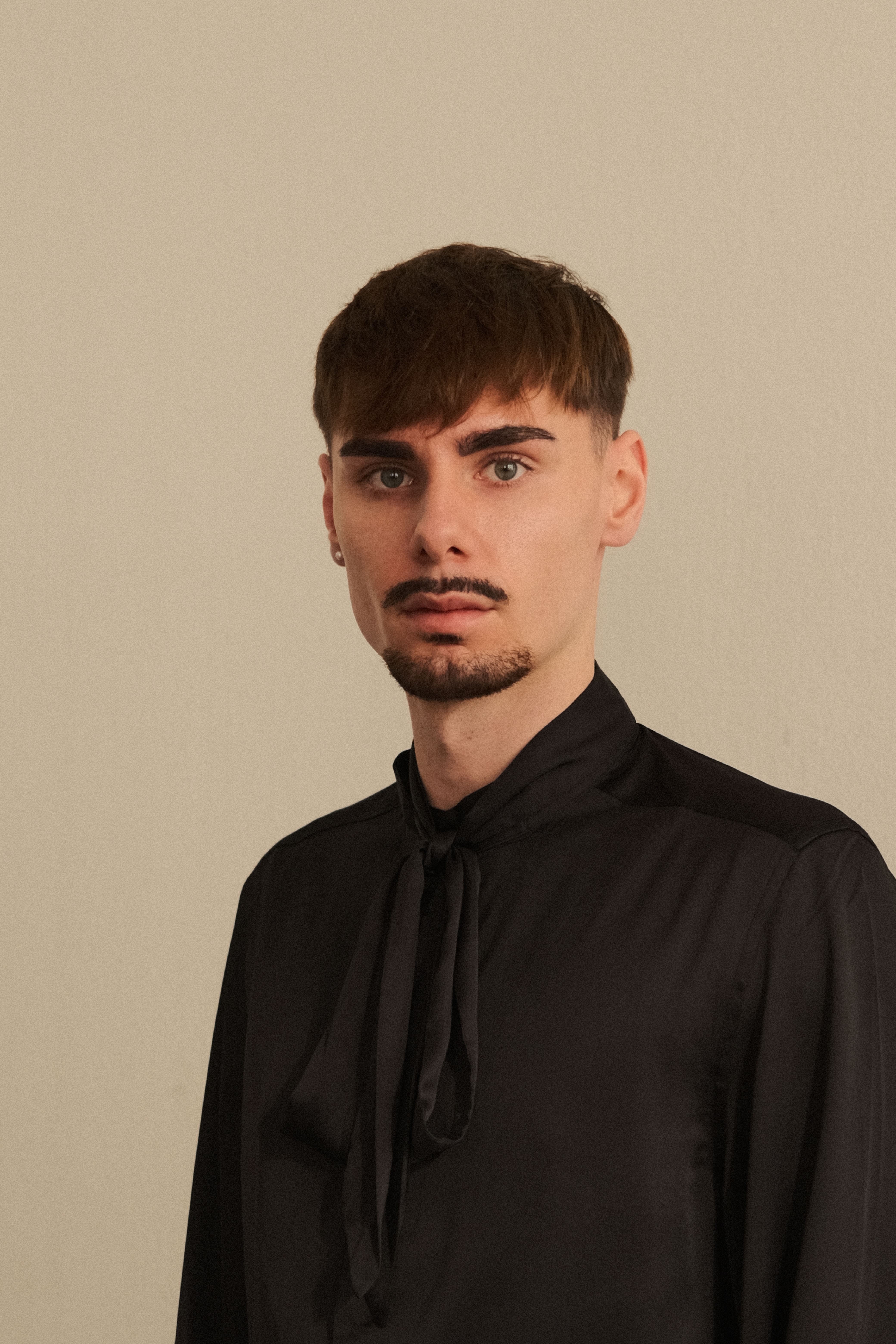 Stylish portrait of a man wearing a black shirt with vintage bow detail against a neutral backdrop.