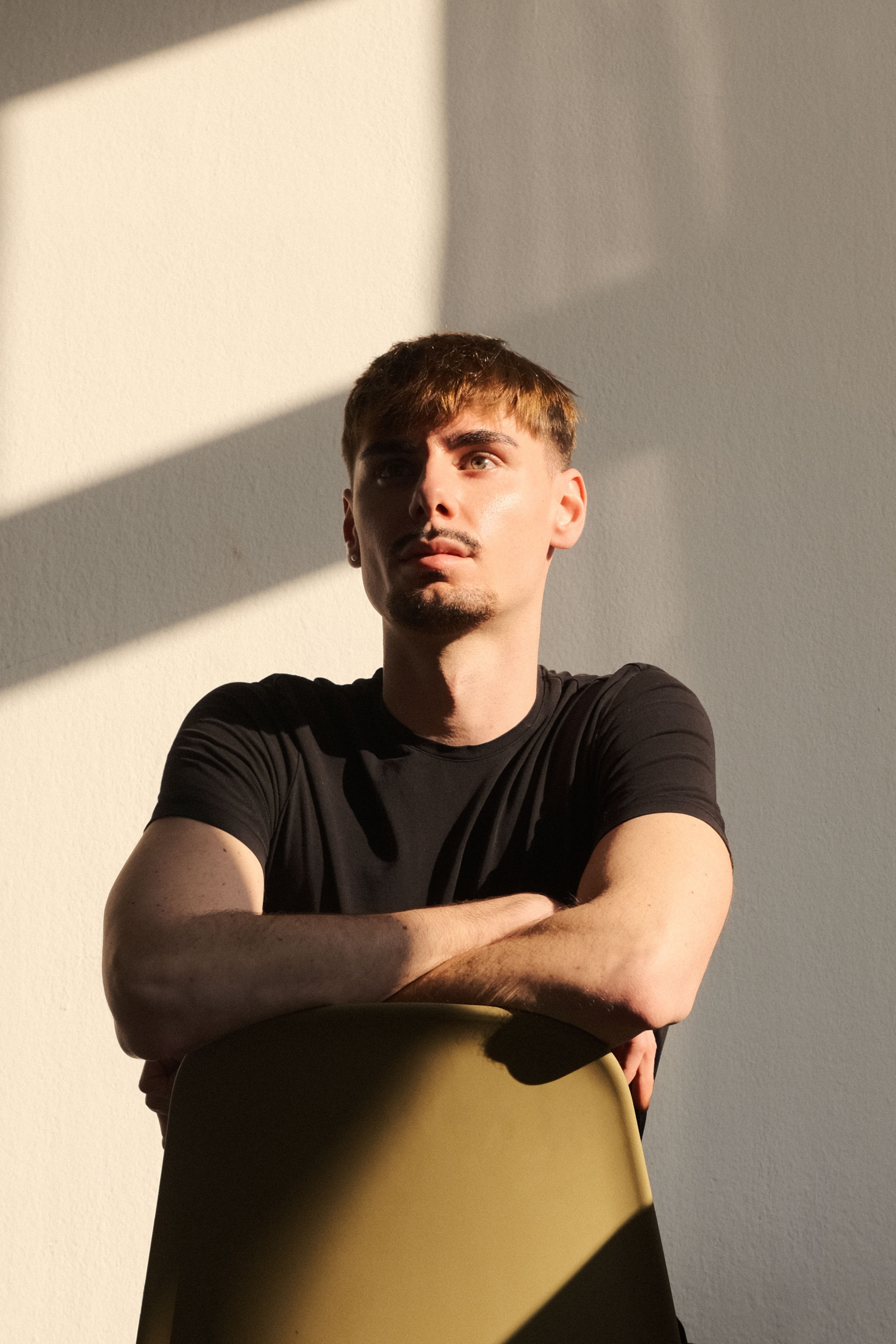 Young man in thoughtful pose, highlighted by dramatic sunlight indoors.