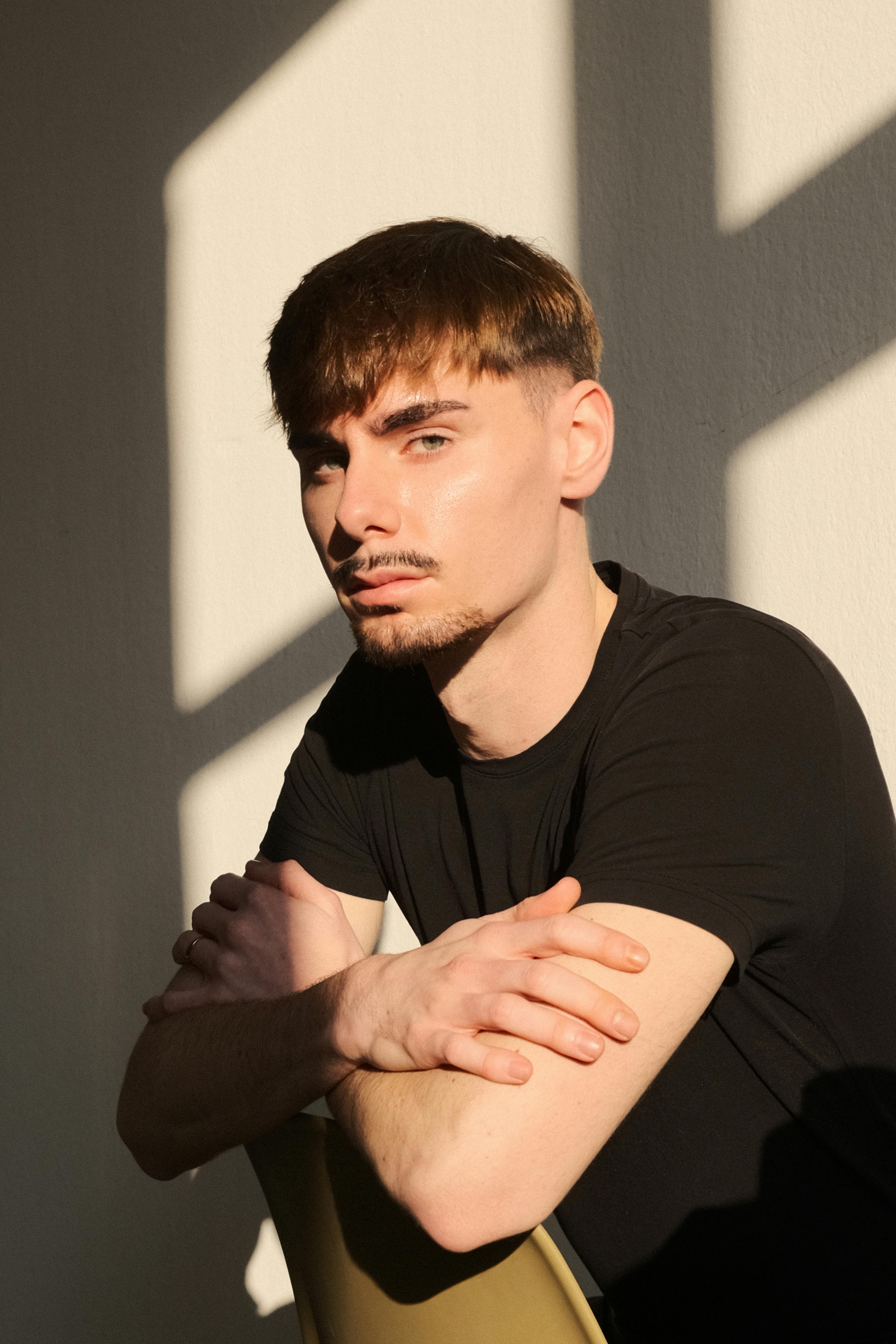 Portrait of a young man in a sunlit room with striking shadows on the wall.