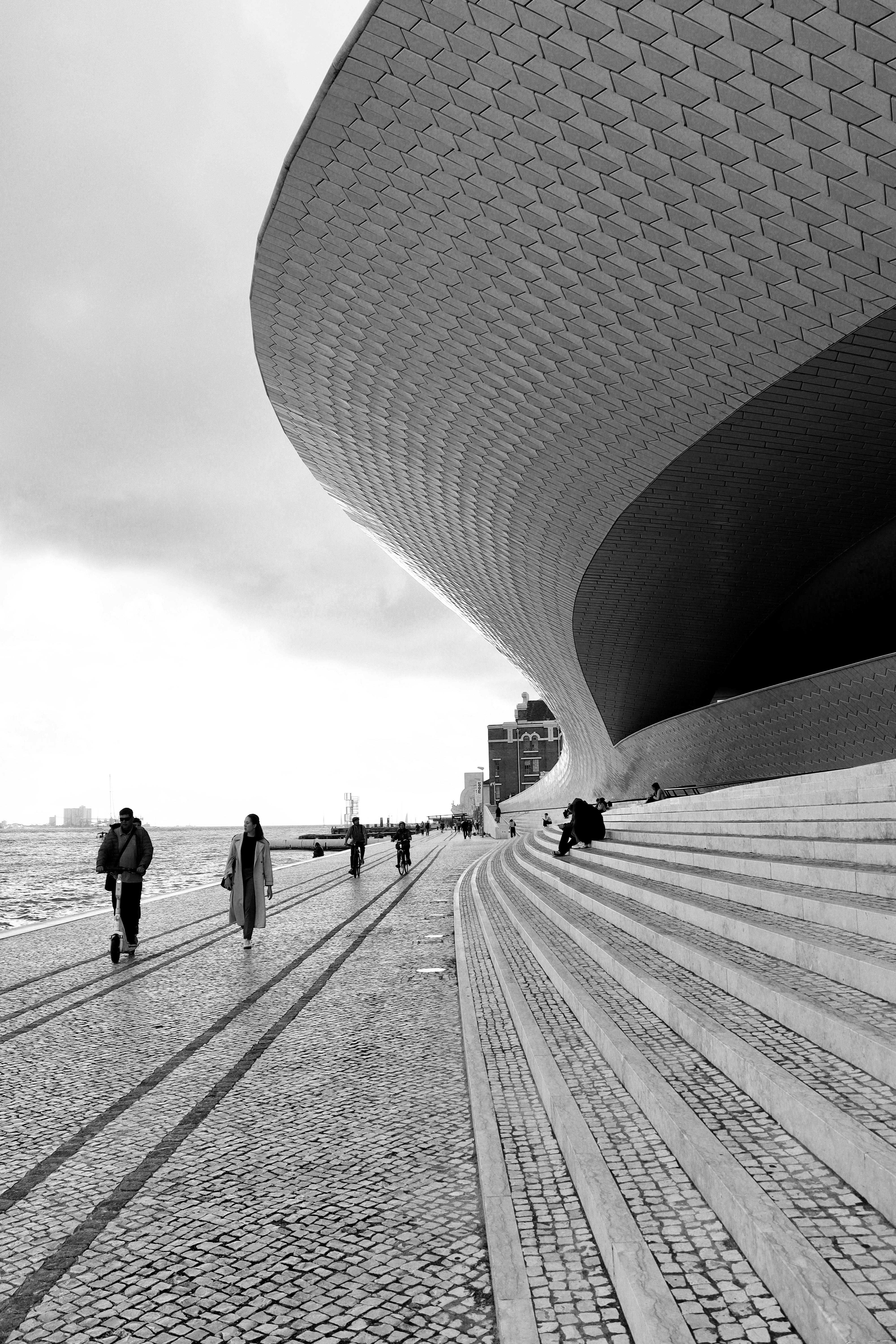 Dramatic black and white architecture along a waterfront with steps and people.