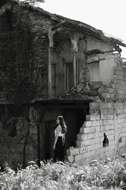 Black and white photo of a woman near an old, crumbling stone house.