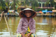 一位身穿传统服装、头戴圆锥帽的越南老妇人在河上