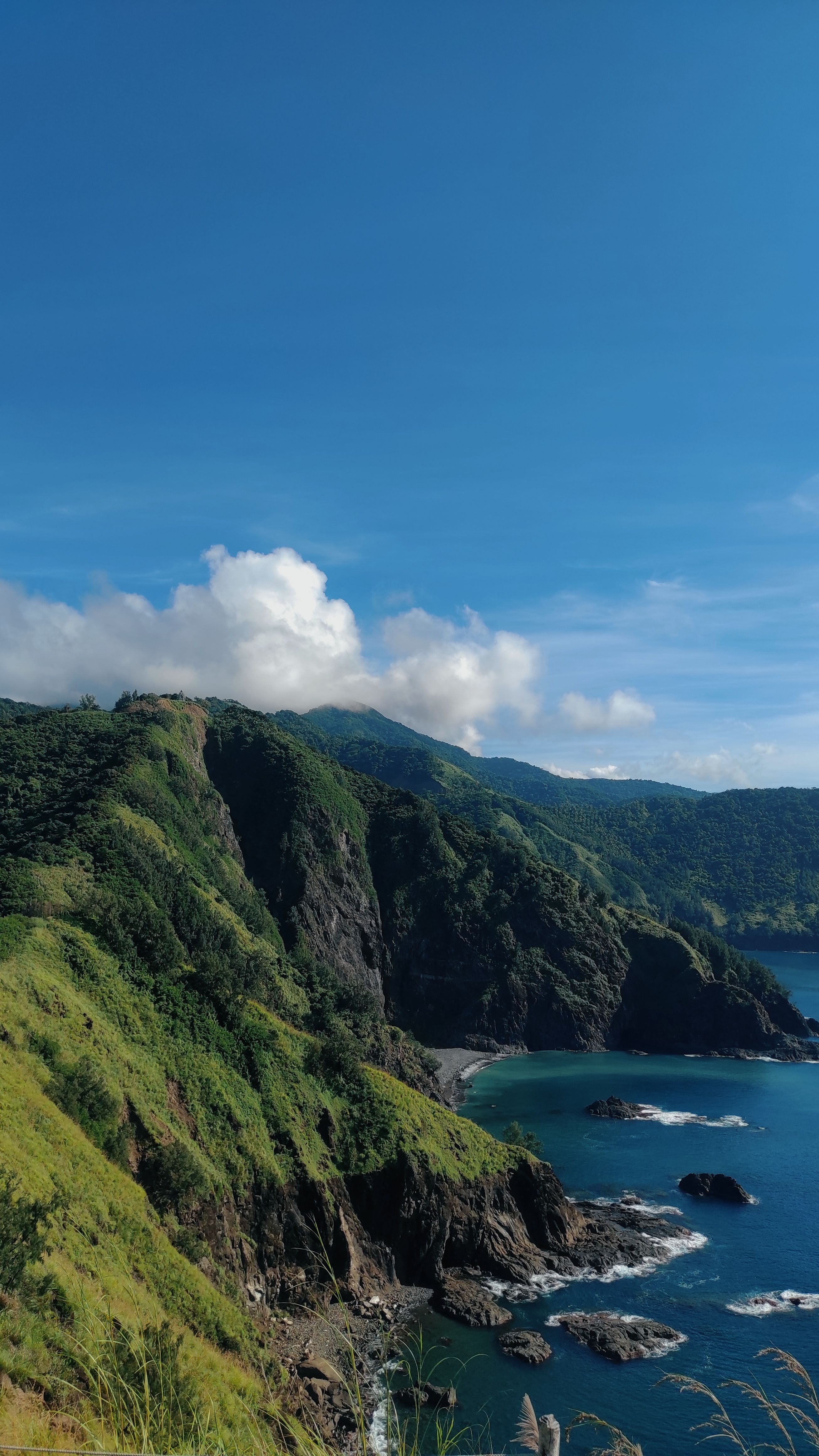 免费 明媚的夏日天空下，郁郁葱葱的山脉和清澈湛蓝的海水，令人叹为观止的海岸景色。 素材图片
