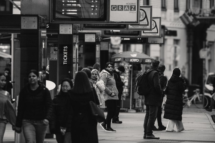 Black and white photo capturing a bustling street scene in Graz, Austria, with people waiting and walking.
