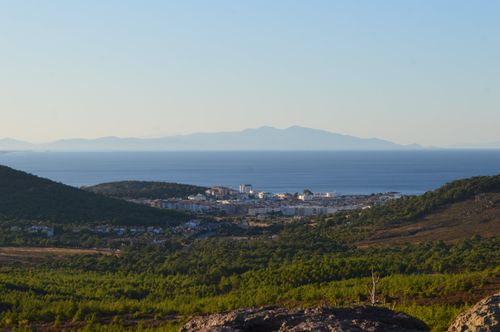 Free A stunning coastal town surrounded by lush green hills against the backdrop of a calm blue sea and distant mountains. Stock Photo