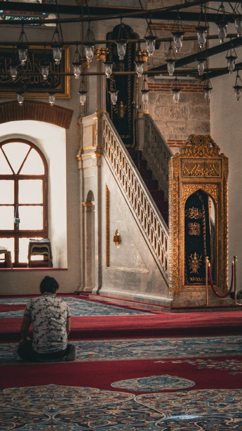 Free A serene scene inside a historic mosque, featuring a single person in prayer, ornate decorations, and a beautifully designed pulpit. Stock Photo