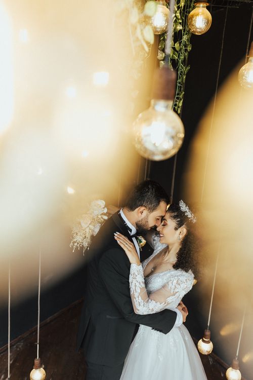 Free Bride and groom sharing a romantic moment under decorative hanging bulbs. Stock Photo