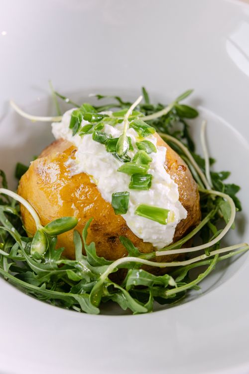 Free Delicious baked potato topped with cheese and greens, served on a white plate. Stock Photo