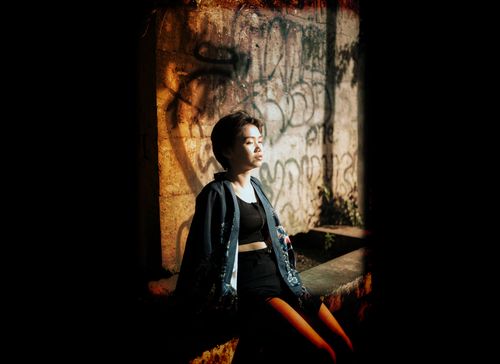 Free A fashionable woman sits against a graffiti-covered wall, basking in sunlight, showcasing urban style and attitude. Stock Photo