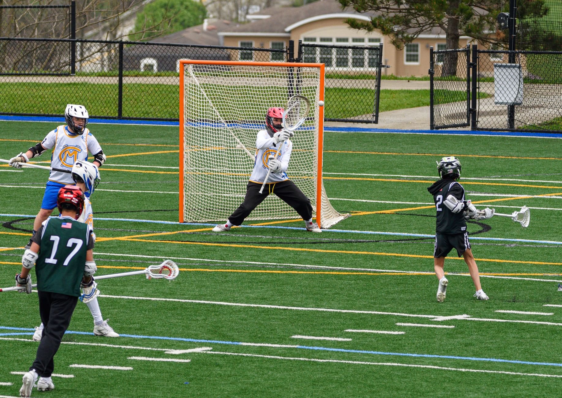 Action-packed youth lacrosse game with players in full gear on a green field.