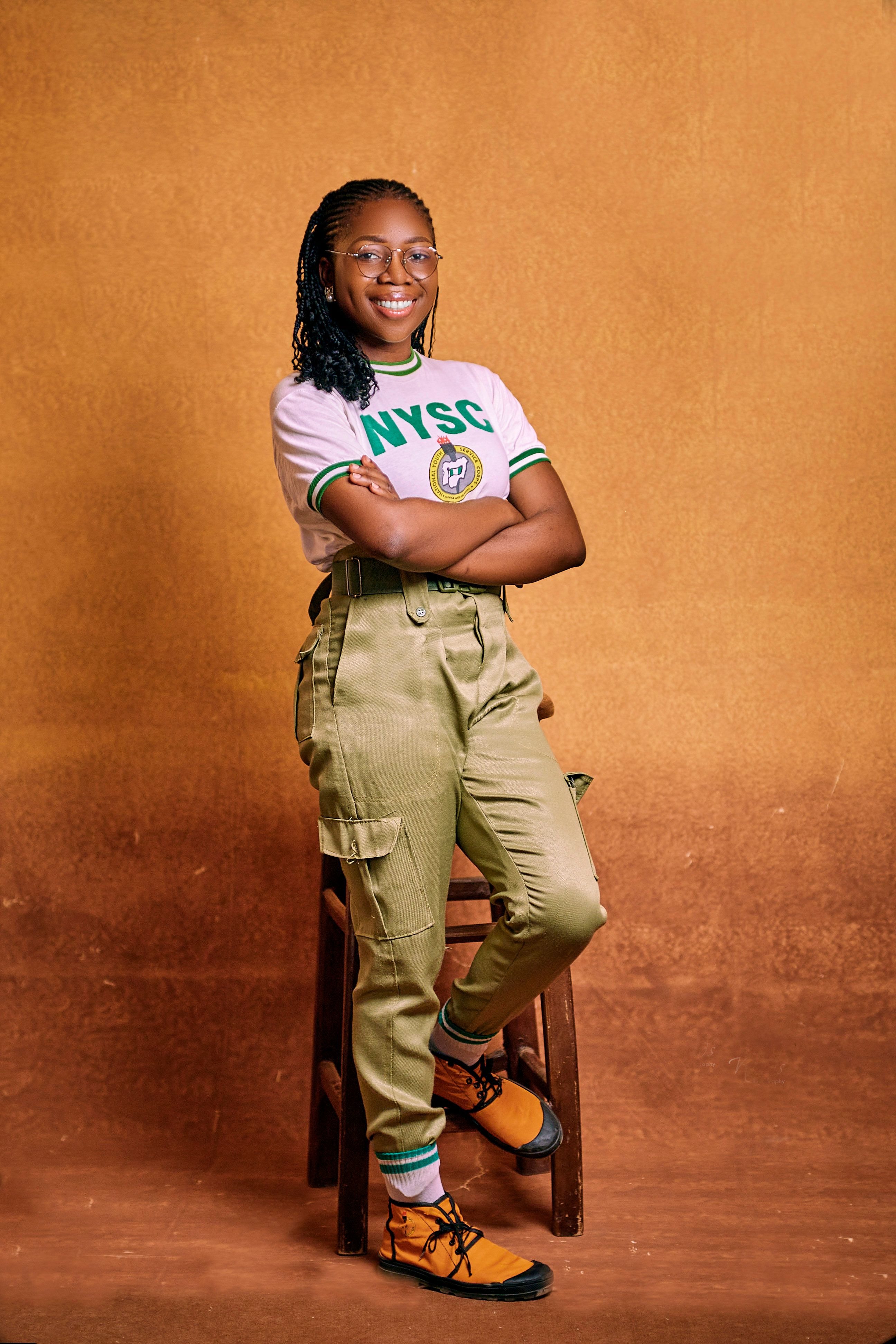 Young adult standing confidently in NYSC uniform against a warm-toned background.
