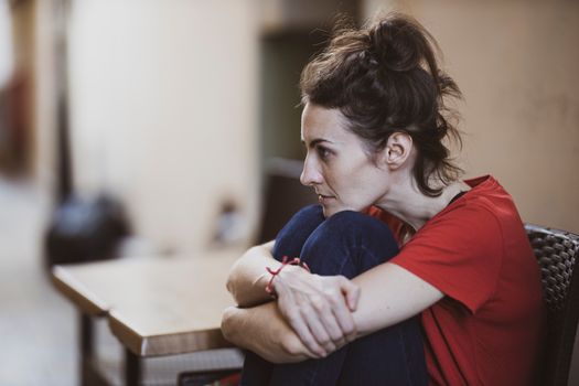 A contemplative woman in casual clothes sits indoors, deep in thought.