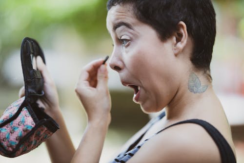 Woman Wearing Black and Gray Tank Top Putting Makeup While Holding Compact Mirror