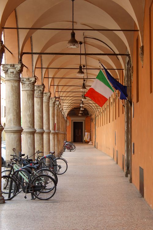 Free A scenic view of Bologna's historic portico with bicycles and Italian flag. Stock Photo