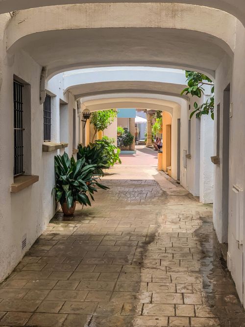 Free Charming sunny alley with arched passage and potted plants, perfect for travel imagery. Stock Photo