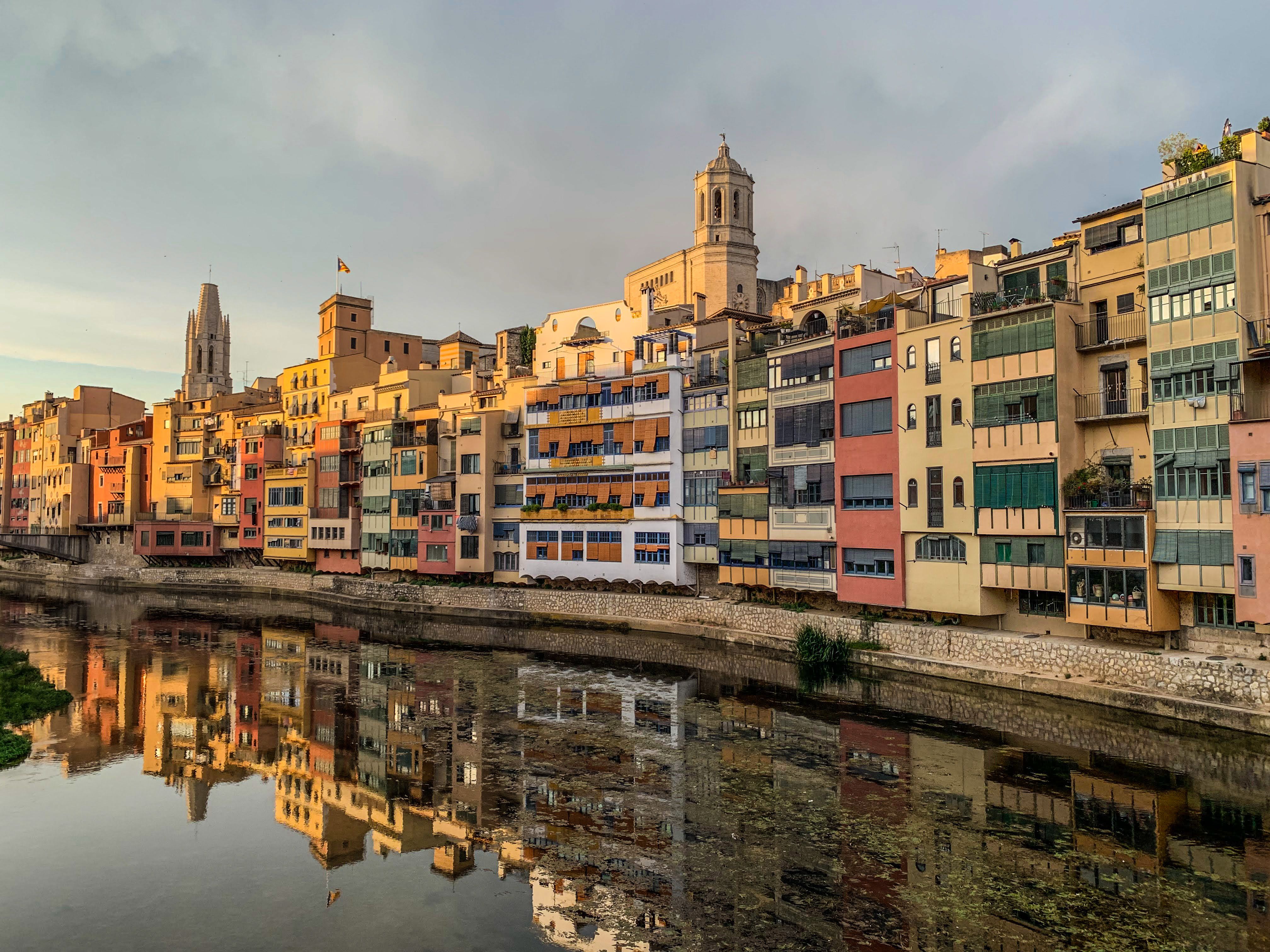 Colorful riverside buildings in Girona reflecting on the river at sunset.