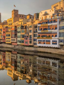 Colorful buildings reflecting in the river during sunset in Girona, Spain.
