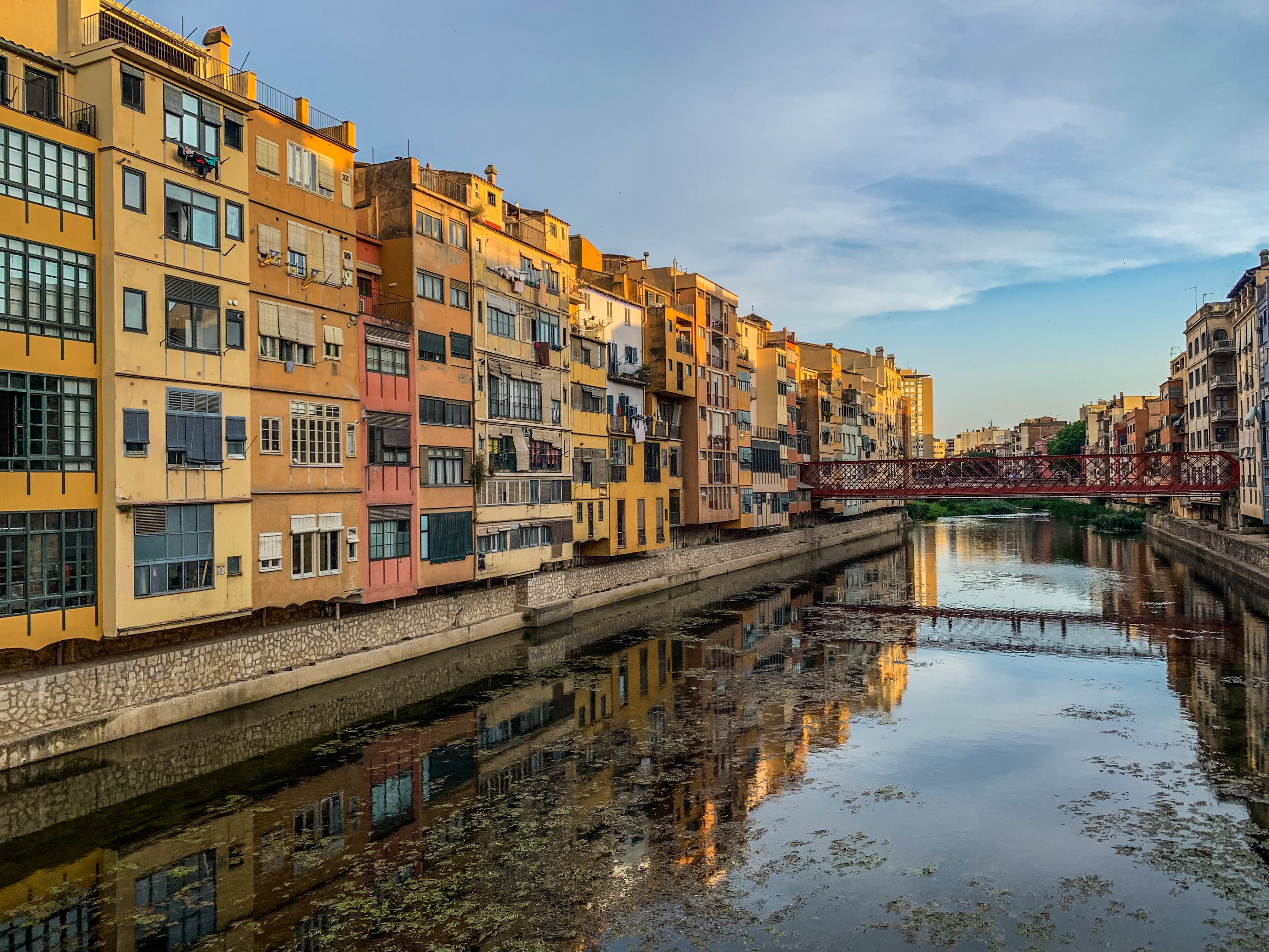 Stunning view of colorful buildings reflecting in the Onyar River at twilight in Girona, Spain.