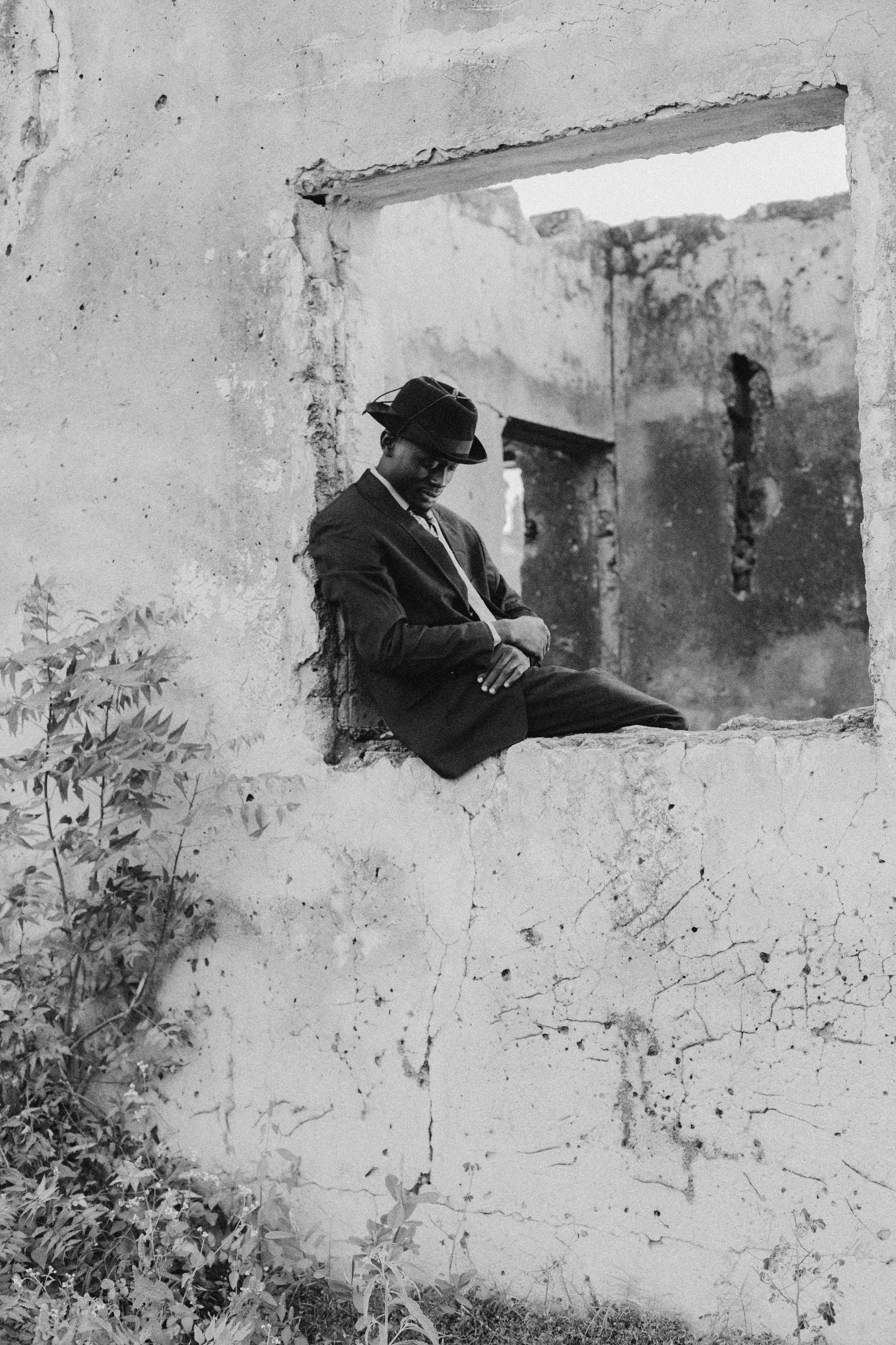 Black and white portrait of a person sitting in a window of a ruined building.