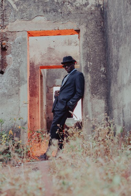 Free A stylish man in a suit and hat poses confidently in an old, rustic building doorway with a dramatic red light ambiance. Stock Photo