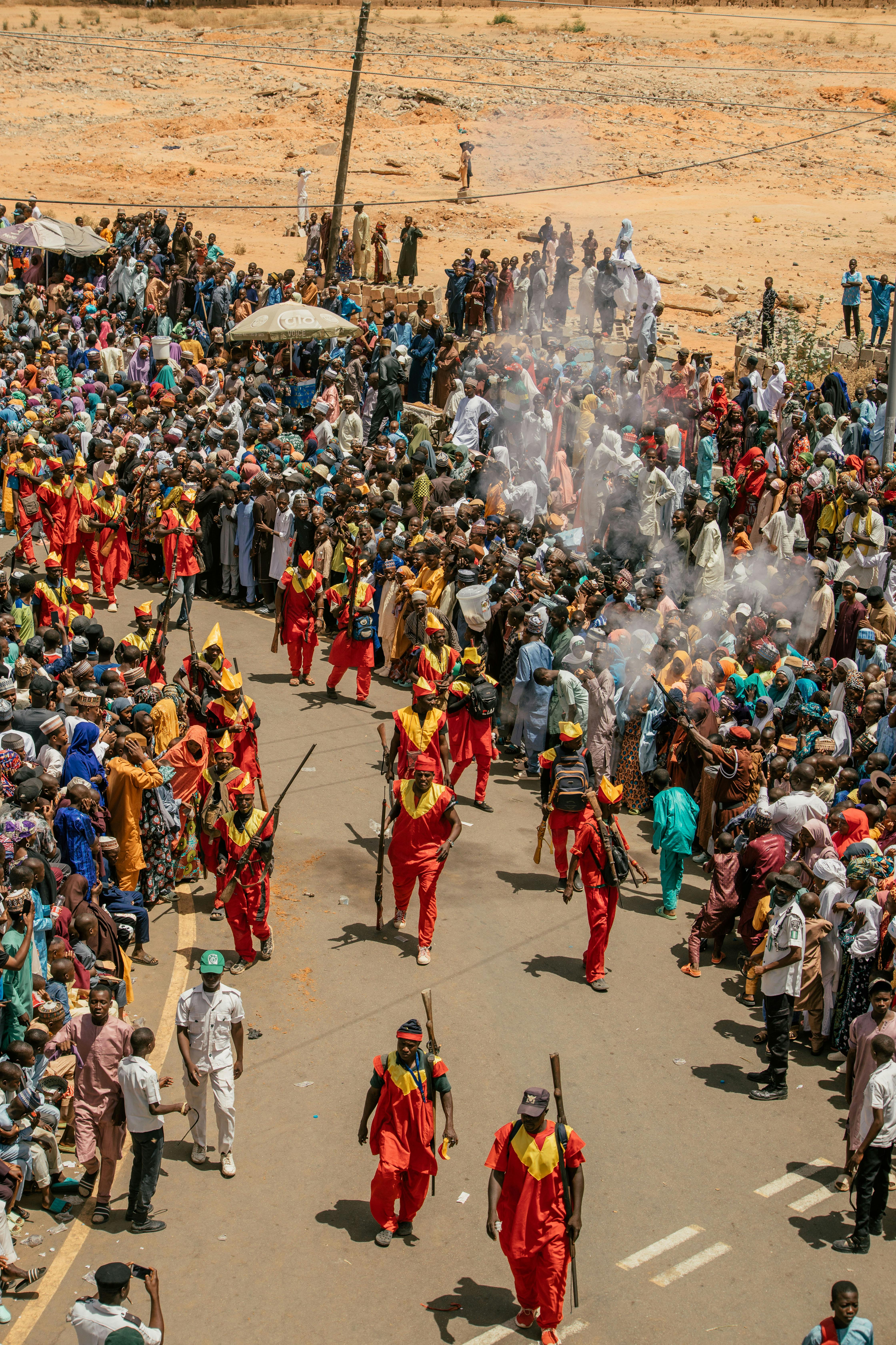 Aerial view of a lively cultural parade with participants in vibrant costumes surrounded by a large crowd.