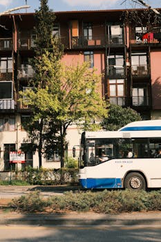 A city bus travels beside an urban residential building covered in plants.