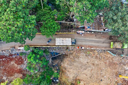 Aerial drone shot of a dirt road in South Tangerang, showcasing lush greenery and construction debris.