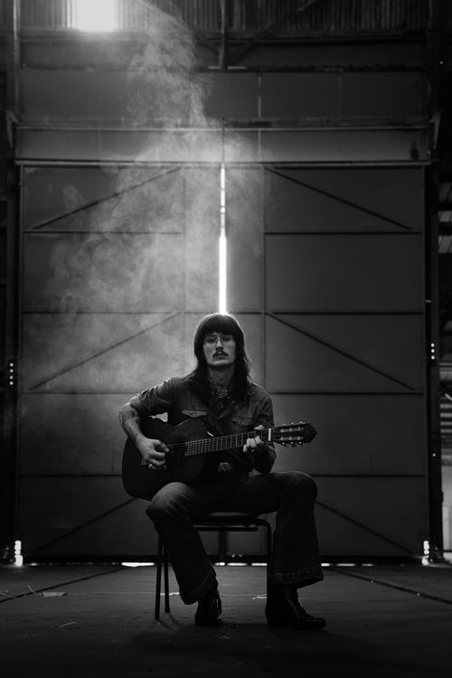 Free Moody black and white image of a musician playing guitar in a dramatic indoor setting. Stock Photo