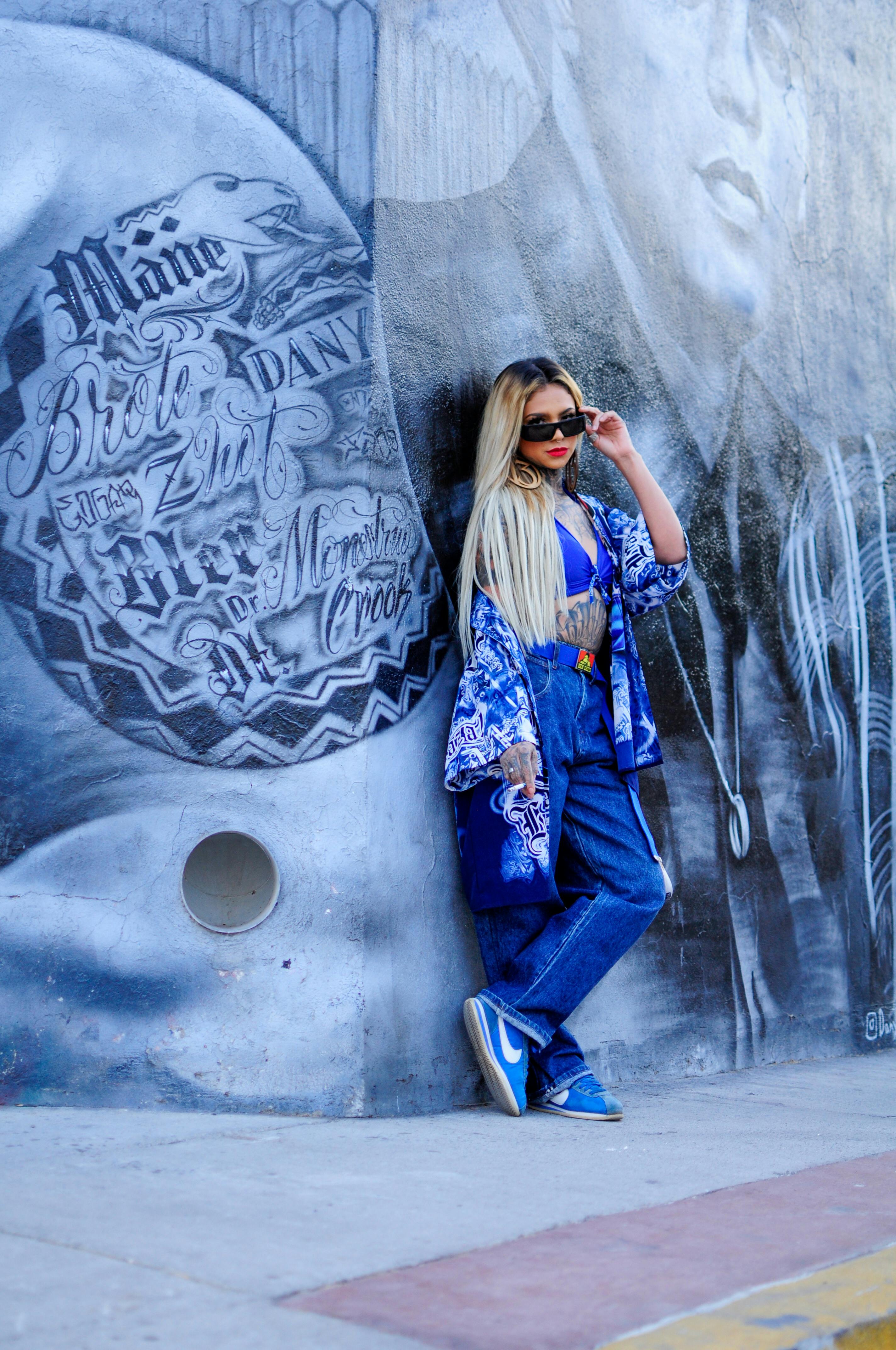 Fashionable woman in blue outfit poses by a graffiti wall showcasing urban street style.