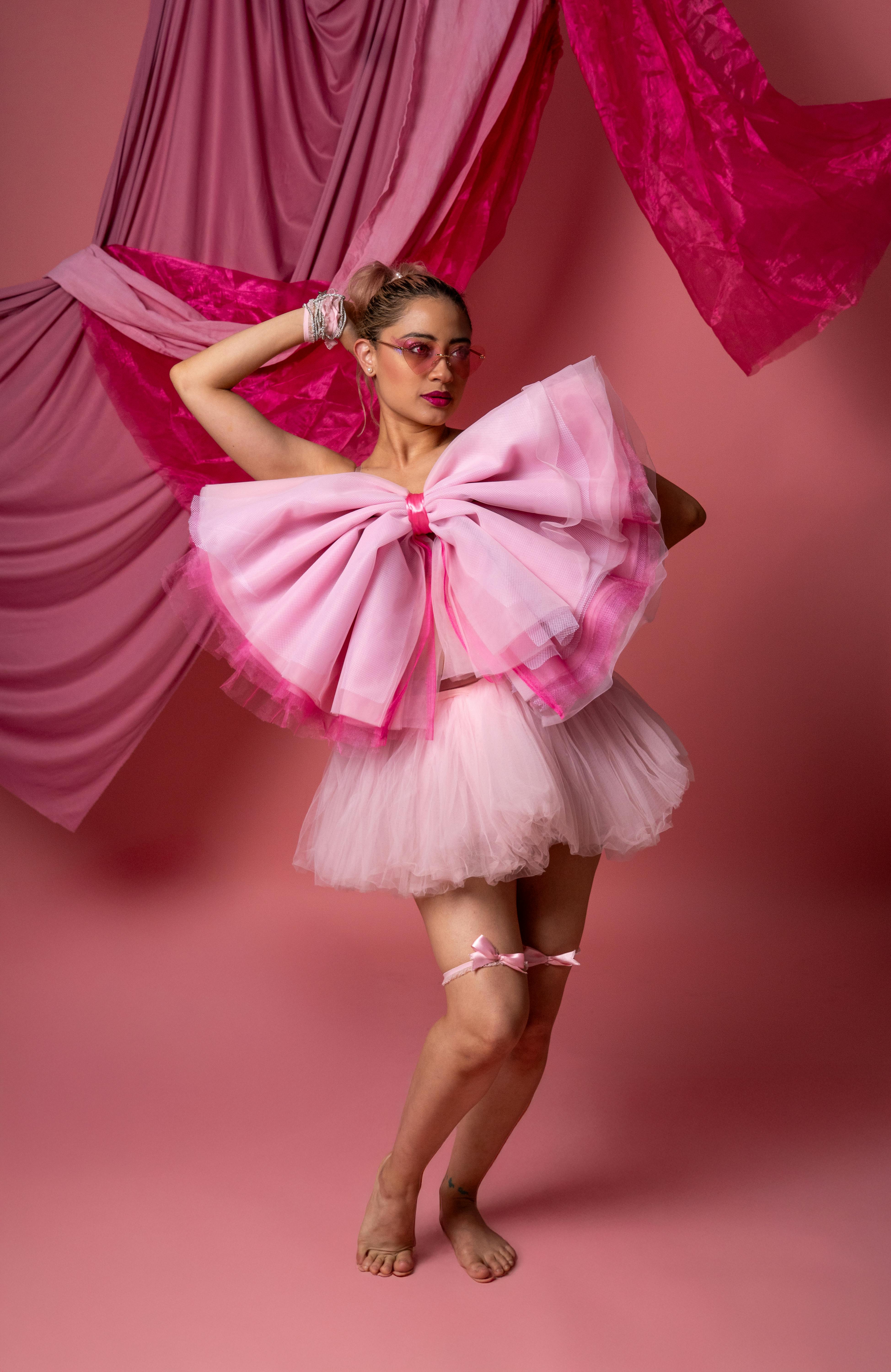 Ücretsiz Çağdaş dansçı, pembe perdeli bir fon önünde pembe tül ve büyük fiyonk ile zarif bir şekilde poz veriyor. Stok Fotoğraflar