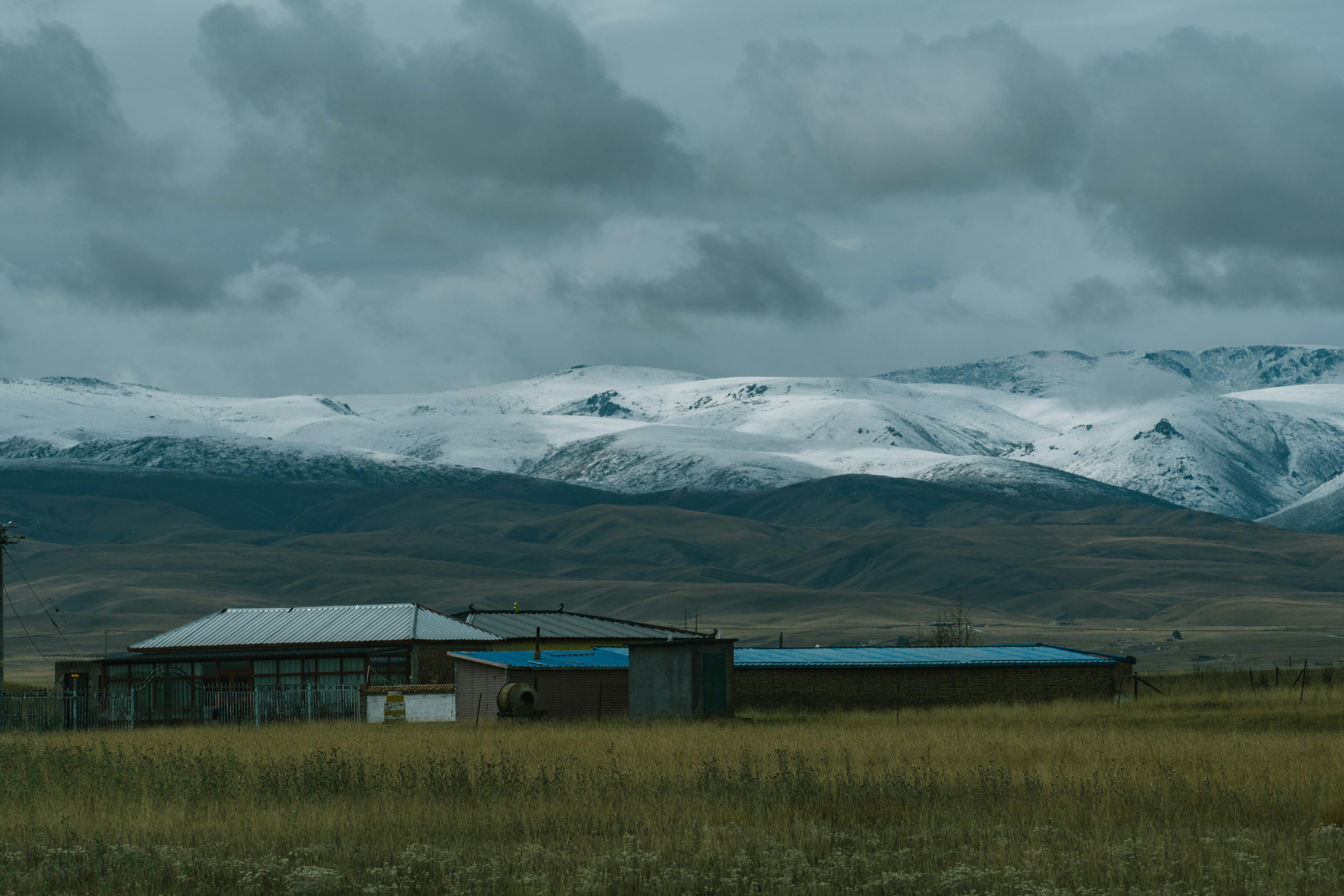 Rural Chinese landscape with snow-capped mountains and cloudy skies, offering tranquility.