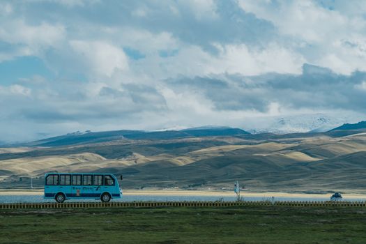 Blue bus travels across vast grasslands against rolling hills in Tibet, China.