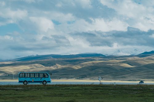 Free Blue bus travels across vast grasslands against rolling hills in Tibet, China. Stock Photo