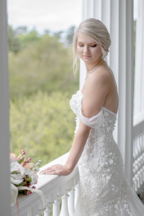 站在白色阳台旁边的女人穿着白色的婚纱