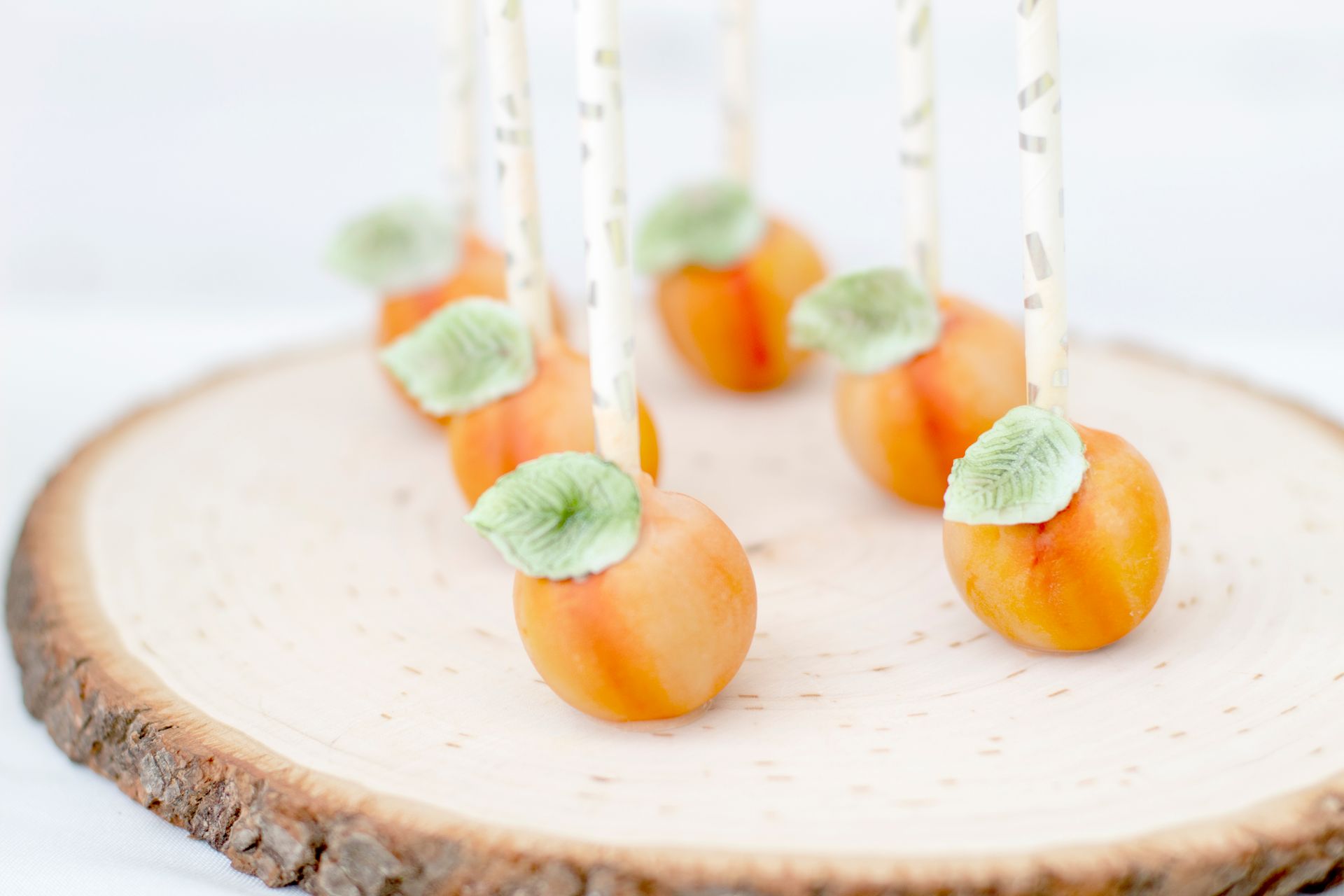 Artistic peach cake pops with leaves on a rustic wood slice, perfect for gourmet events.