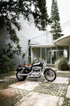 A sleek motorcycle parked beside a contemporary house with lush greenery.
