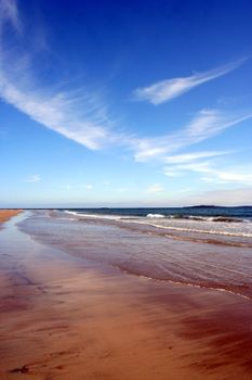 Tranquil beach scene with gentle waves and blue skies in Seahouses, UK.