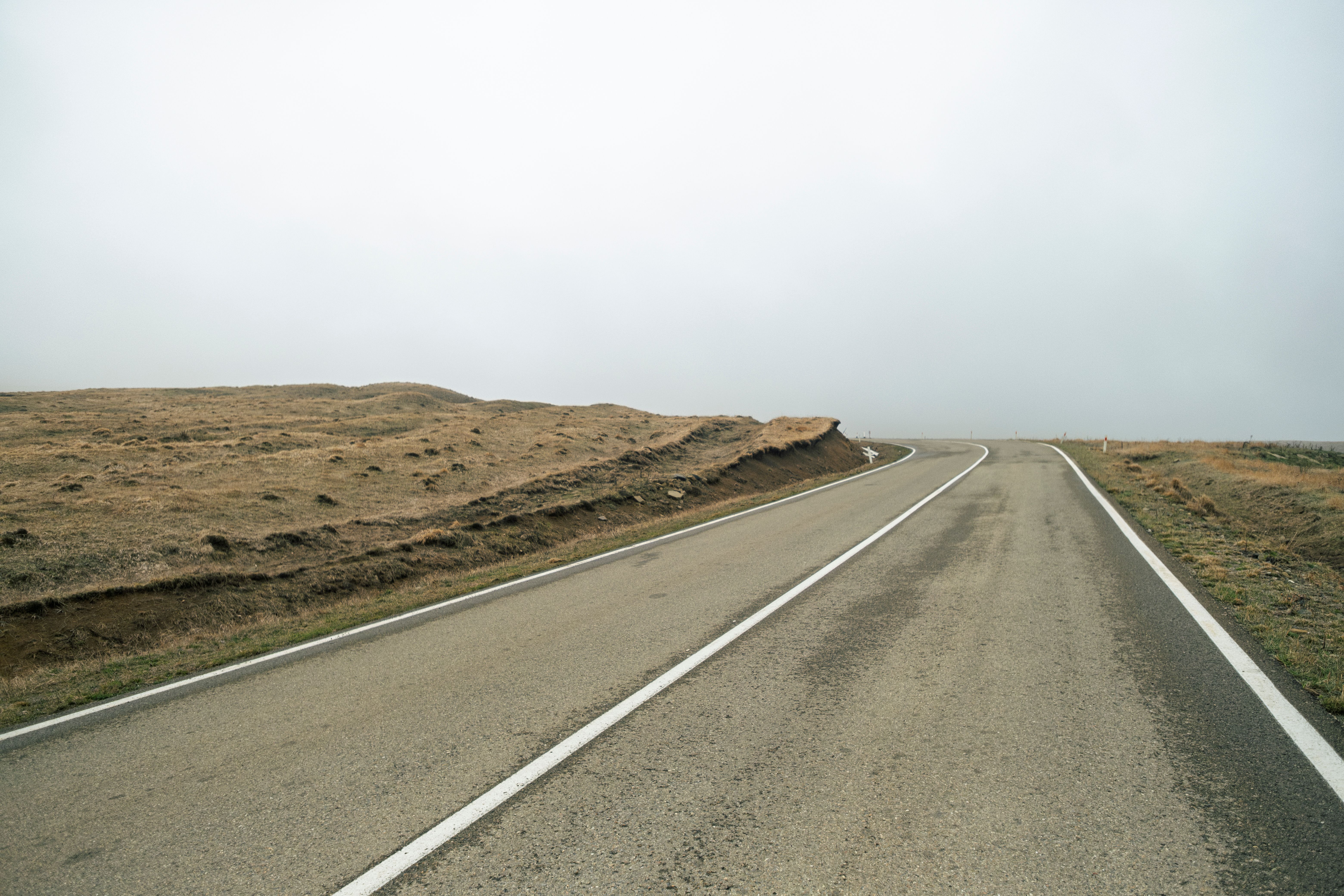 A quiet, solitary road through open, barren terrain under a cloudy sky.