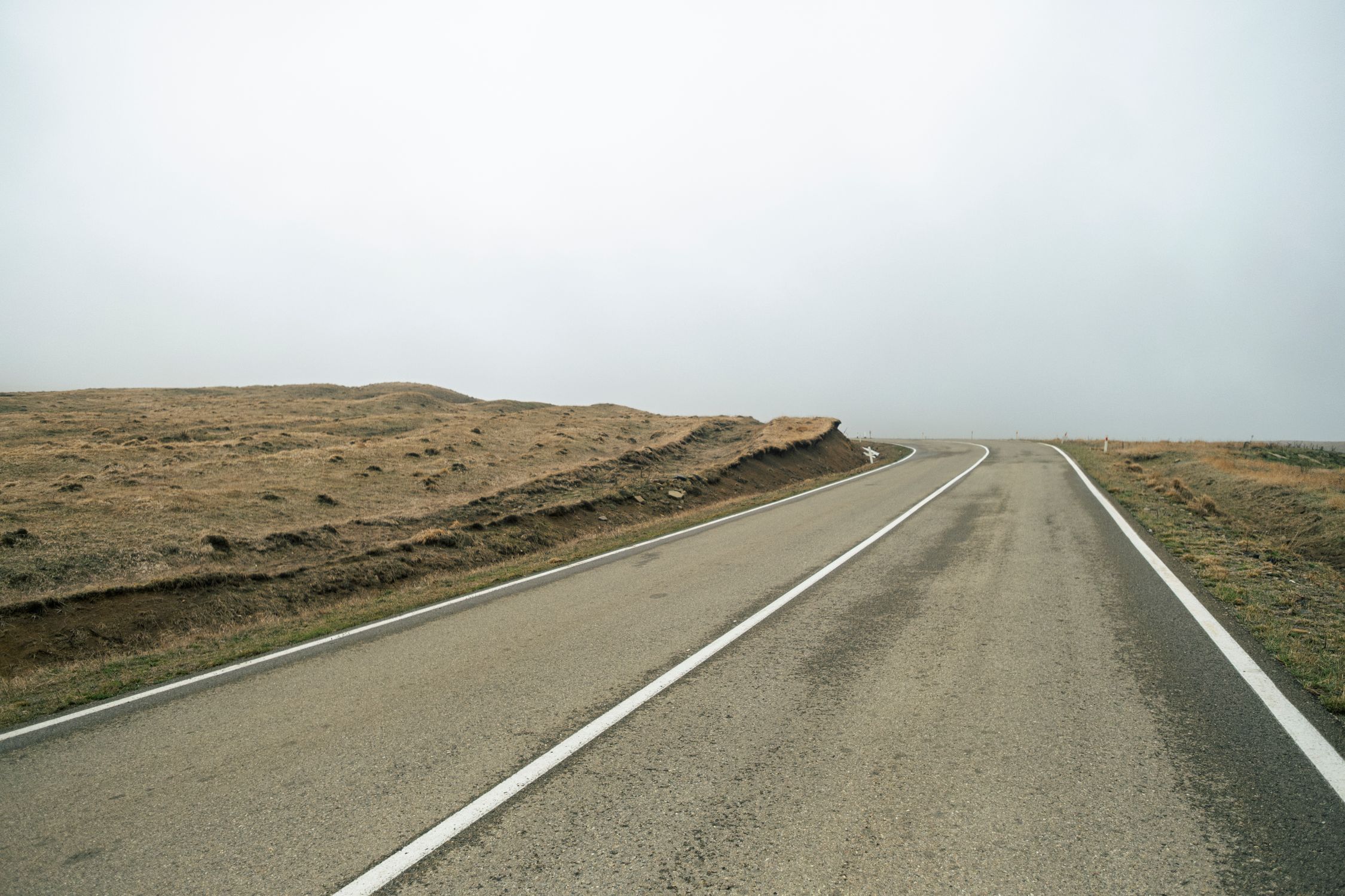 A quiet, solitary road through open, barren terrain under a cloudy sky.