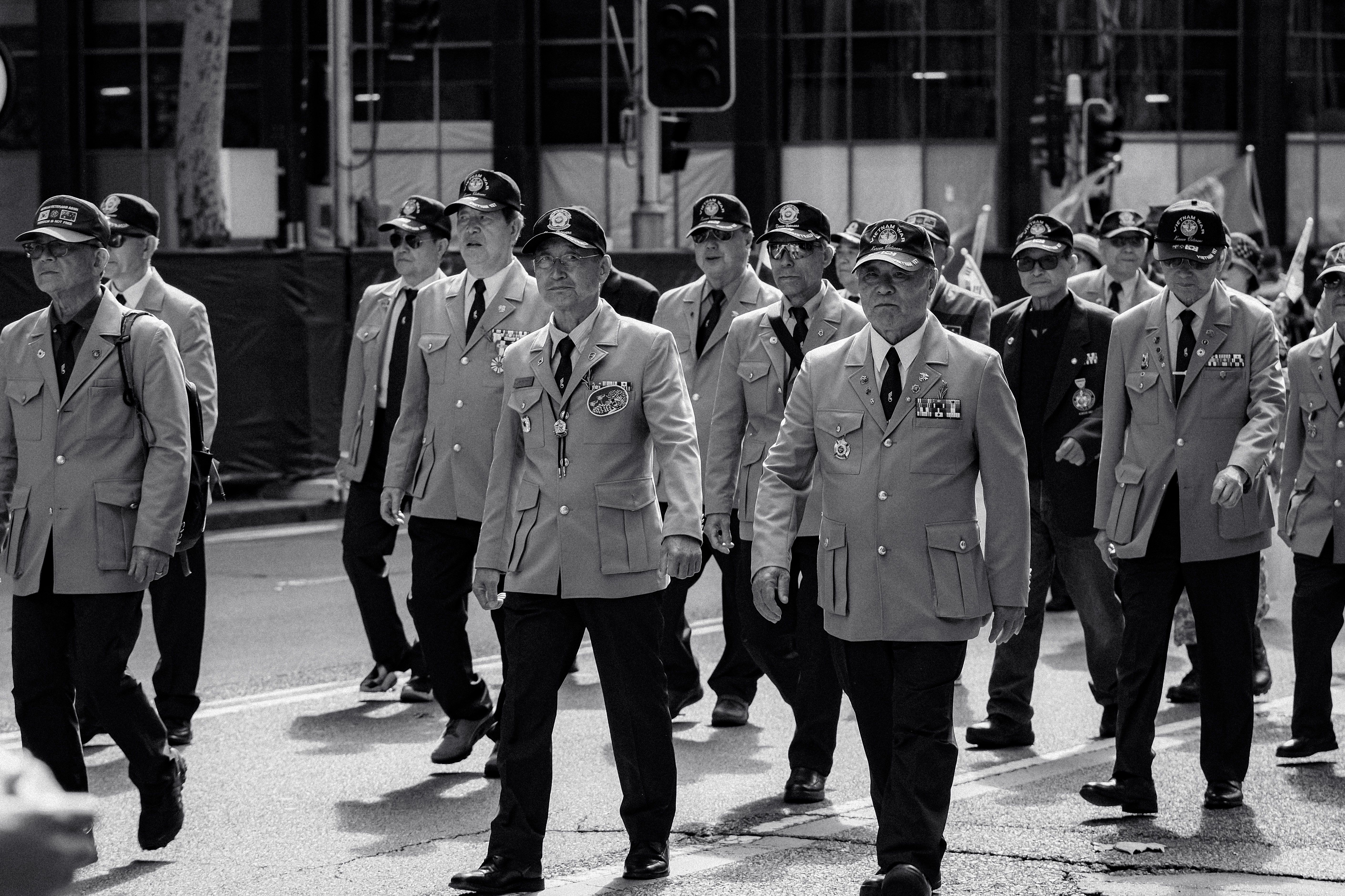 A black and white photo of veterans marching in a city parade wearing medals and uniforms.