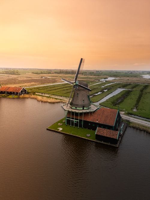 Free Scenic aerial shot of a classic Dutch windmill surrounded by waterways during sunset in the Netherlands. Stock Photo