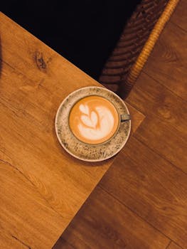 Top view of a cappuccino with latte art on a wooden table in a cozy cafe setting.