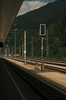 A serene railway station overlooking lush green mountains under a cloudy sky.