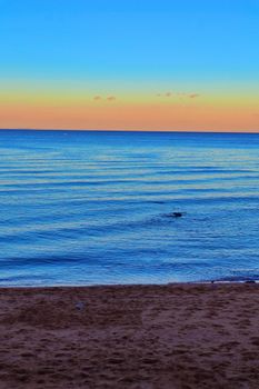 Tranquil beach scene at sunset with orange and blue sky over calm ocean waters.