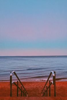 Tranquil beach scene with a staircase leading to calm ocean waters and a vibrant sky.