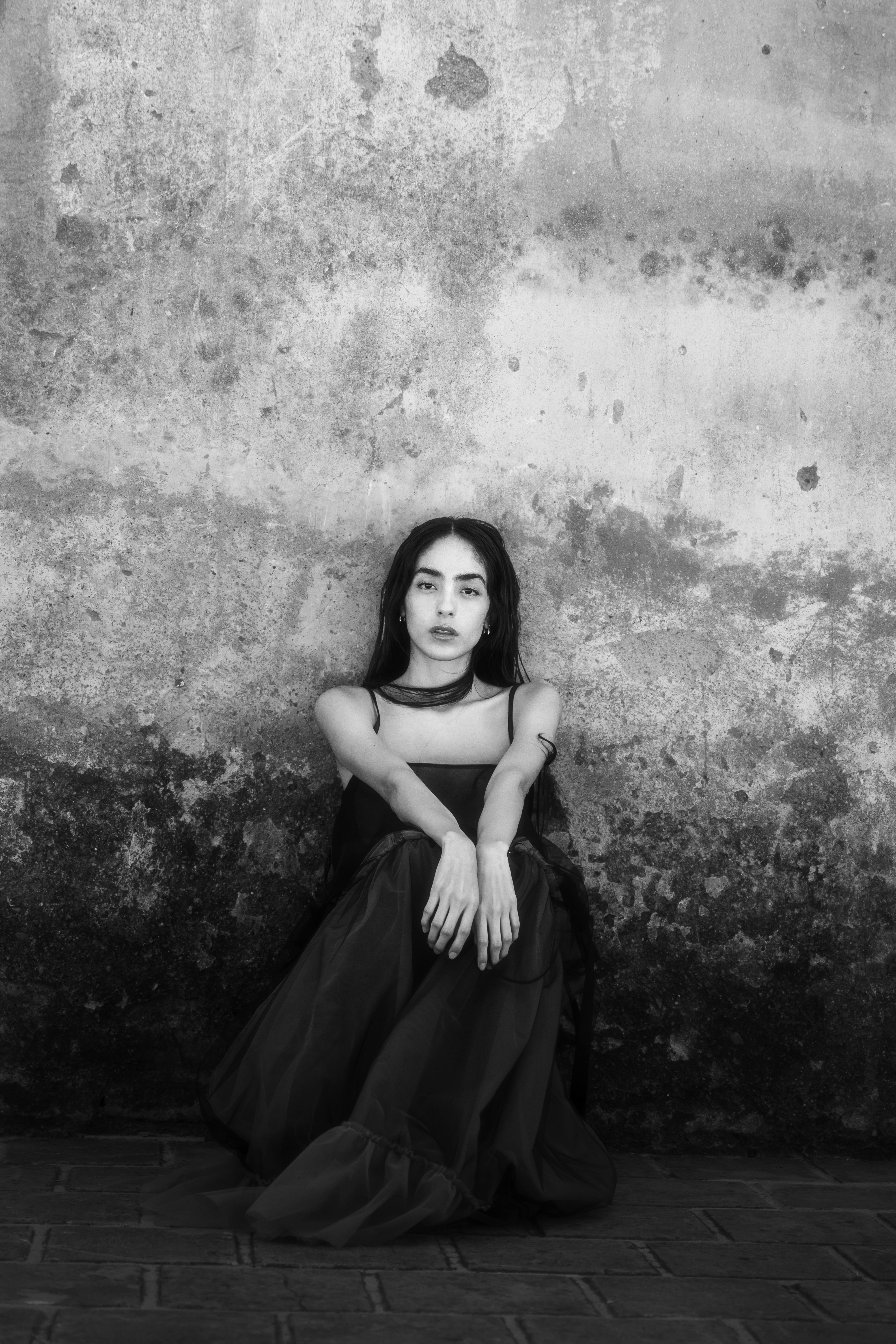 bezplatná Nápadný černobílý portrét ženy sedící u texturované zdi. Základová fotografie
