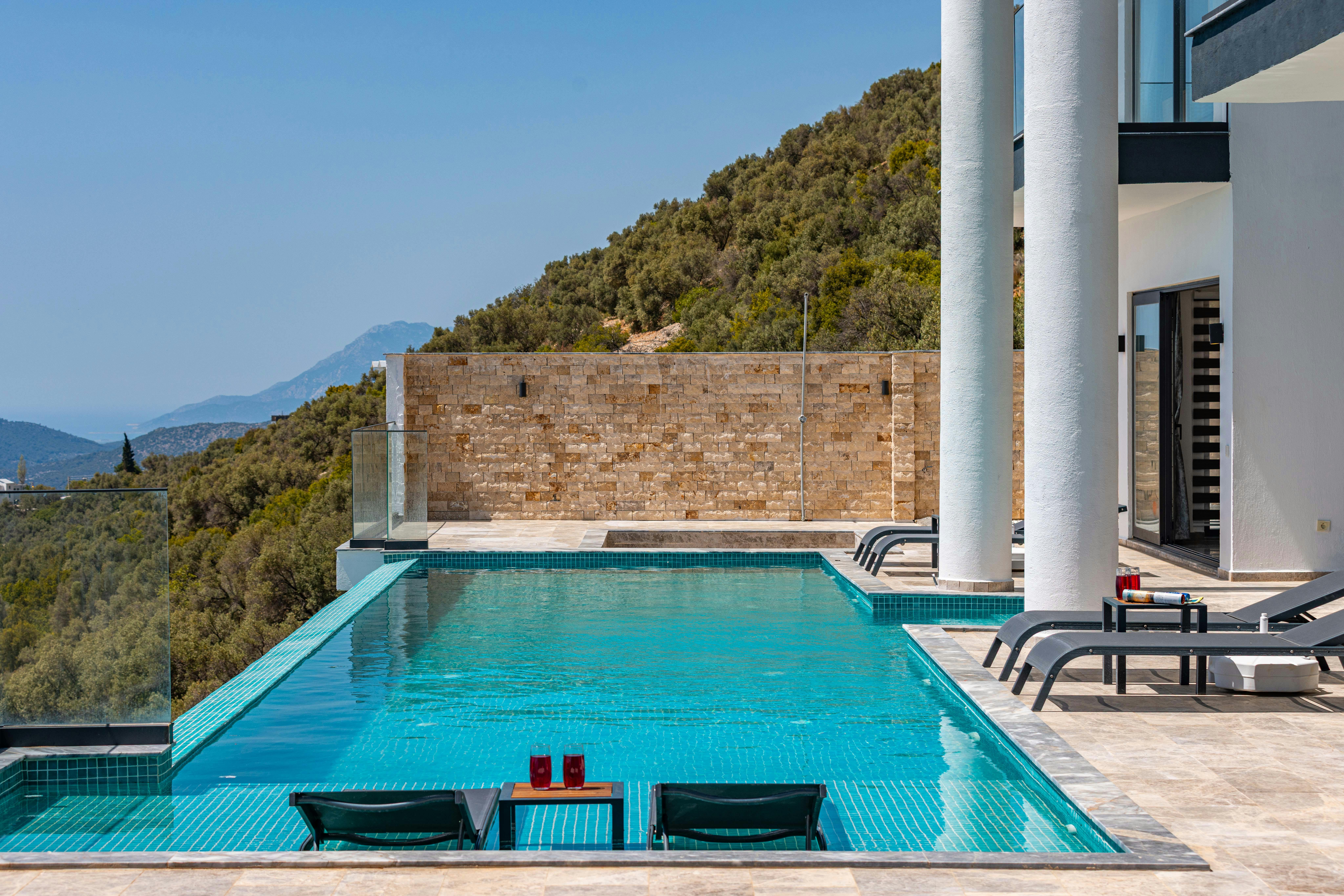 Piscine à débordement avec vue sur la montagne et chaises longues dans un cadre de villa ensoleillé.