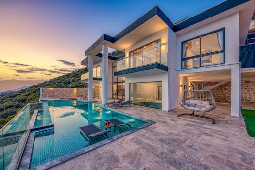 Elegant modern villa featuring an infinity pool and scenic hill views during sunset.