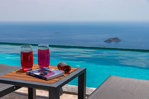Serene poolside view with drinks, book, and infinity pool overlooking the sea.